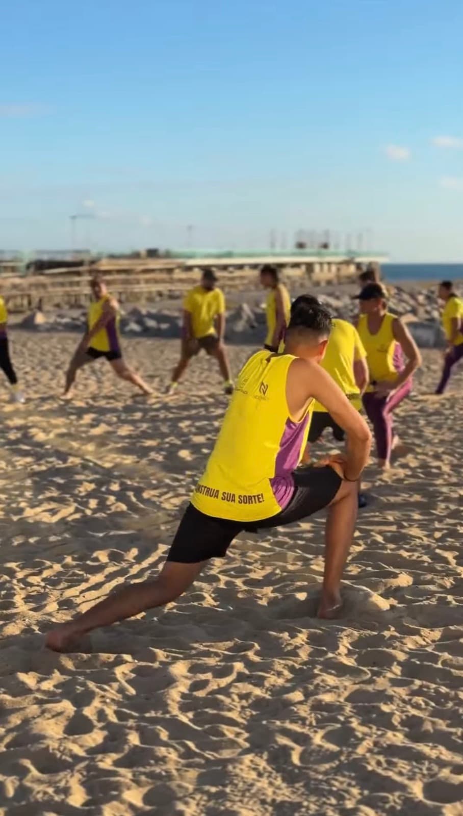 Alongamento na areia com a camisa Construa sua Sorte