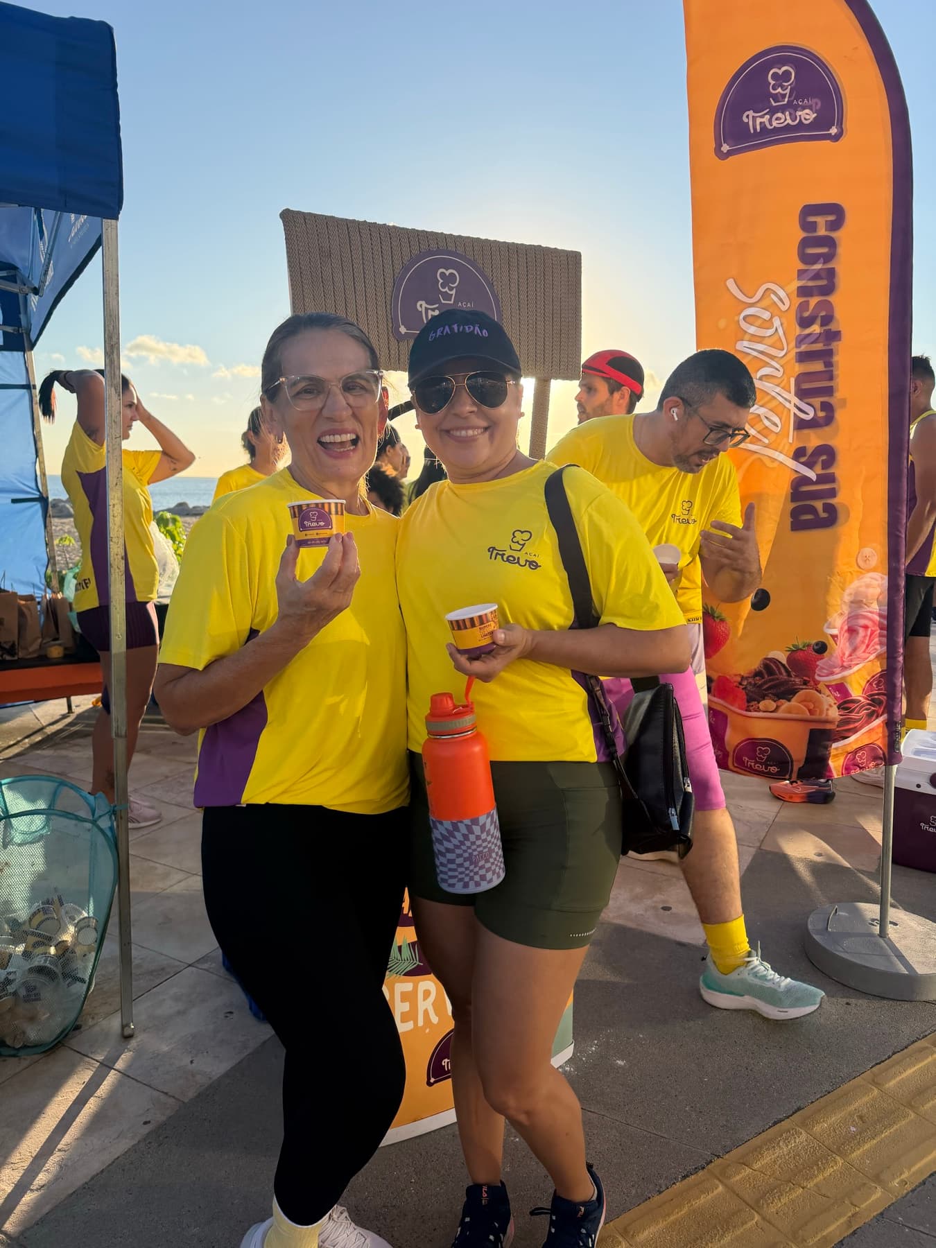 Duas participantes sorrindo com copinhos de açaí Trevo na mão